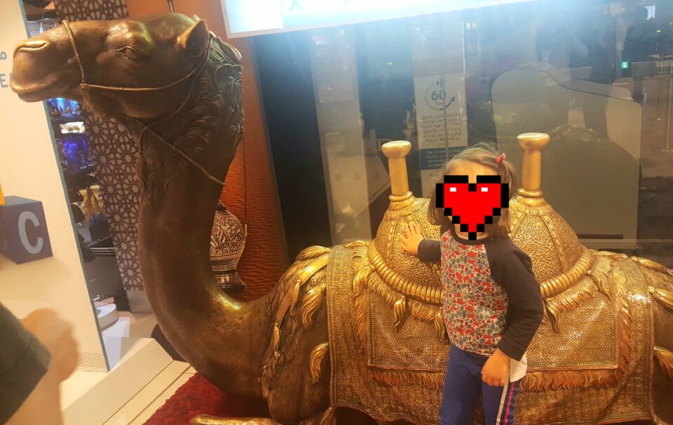 La mia bimba gioca con la statua dorata di un dromedario all'aeroporto di Abu Dhabi