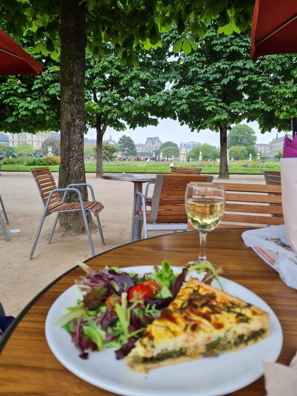 Una fetta di quiche, un bicchiere di vino francese e lo sfondo dei Jardin des Tuileries a Parigi